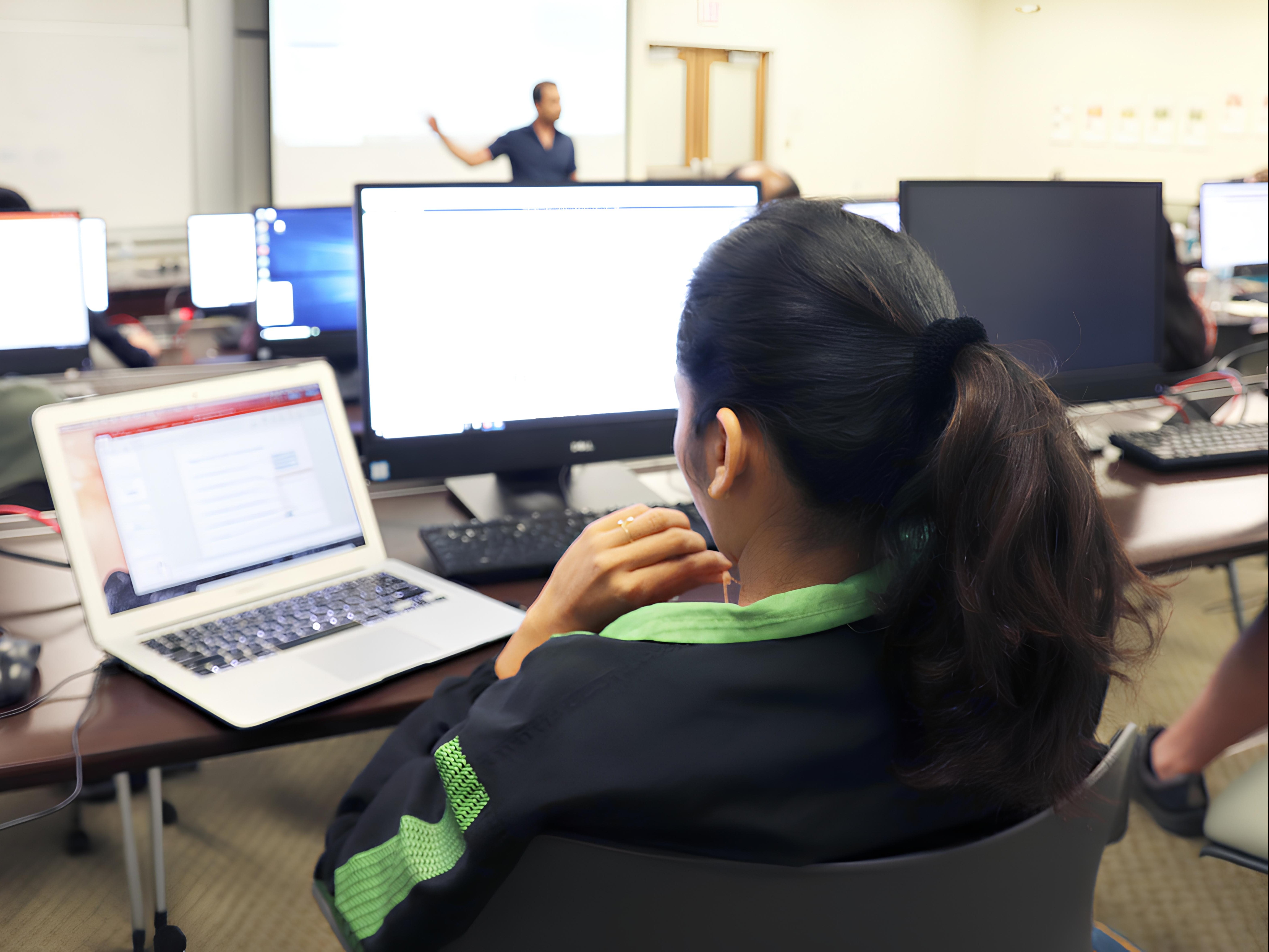 A computational genomics student sits behind a workstation while an instructor teaches