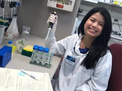 Danielle Yee wearing a white lab coat, sitting in a chair and holding up a large syringe