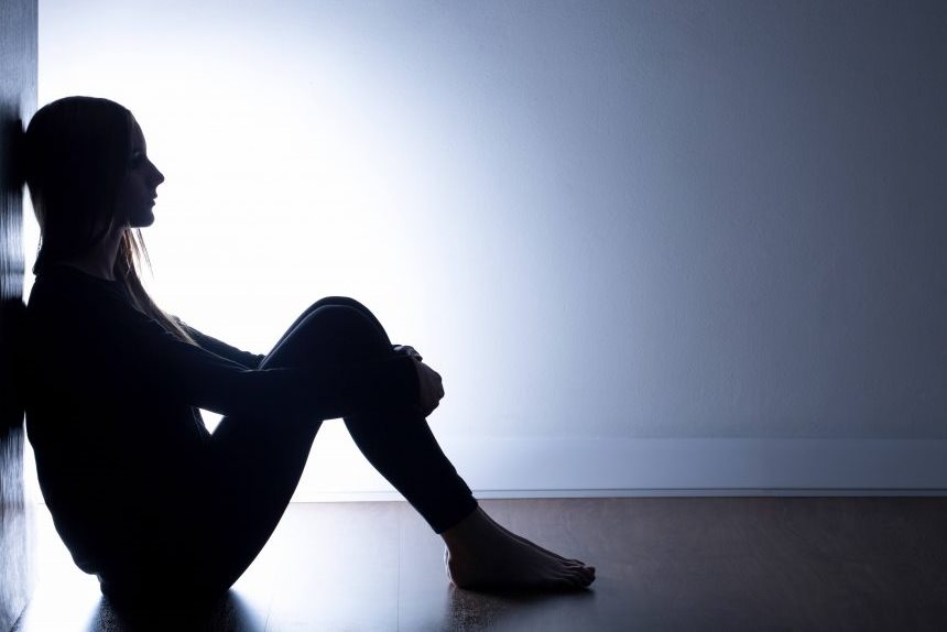 person seated on floor leaning against wall silhouetted by light behind