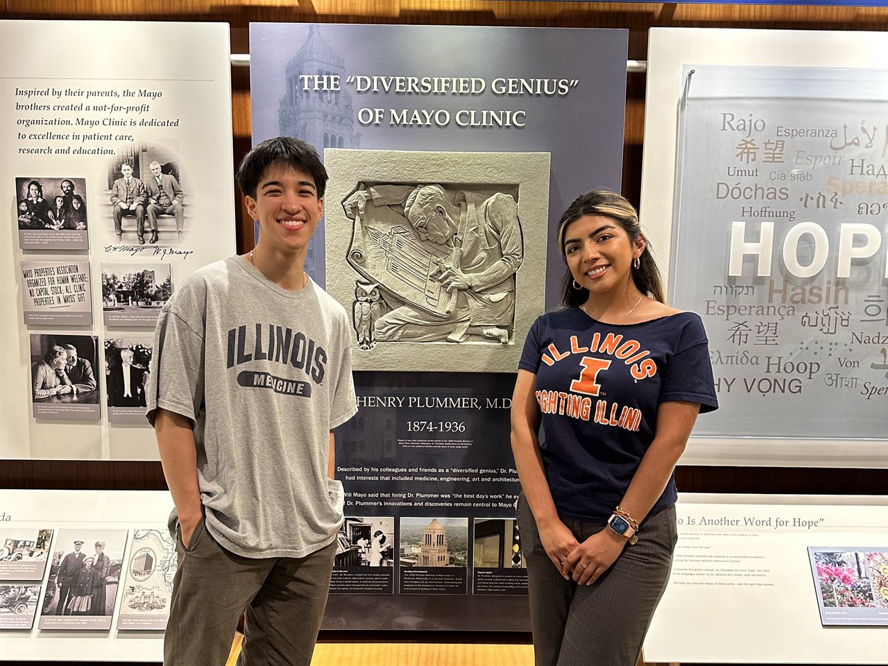 HERE 2023 Cohort Isela and Brandon standing near a Henry Plummer display at Mayo Clinic.